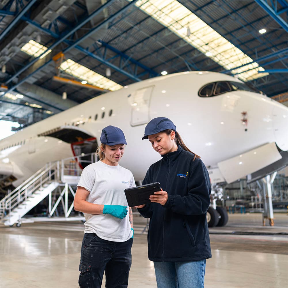 Deux techniciennes de Sabena technics devant un avion dans un hangar, illustrant la maintenance des vols commerciaux
